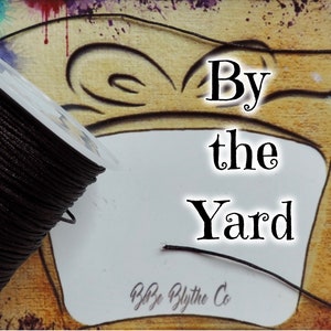 May include: A spool of black cord with the text "By the Yard" and "By the Blythe Co" on a white card.