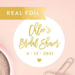 May include: Round white sticker with gold foil text that reads "Chloe's Bridal Shower 6.12.2021" with a small gold heart at the bottom.