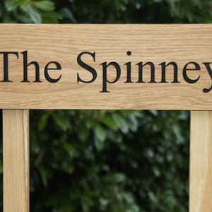 May include: A wooden sign with the text "The Spinney" carved into it. The sign is mounted on two wooden posts.