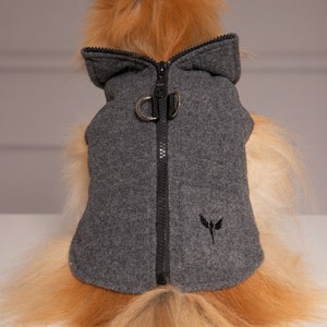 May include: A gray fleece dog coat with a black zipper and a black logo on the back. The coat has a hood and a leash attachment.