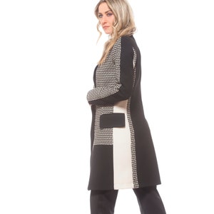 May include: A woman wearing a black and white patterned coat with a black and white geometric design. She is wearing black pants and black heeled shoes.