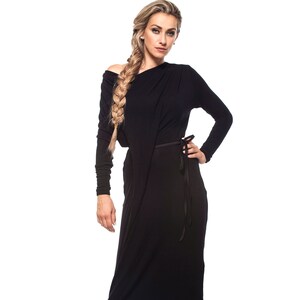 May include: A woman wearing a long black dress with a side tie. She has long blonde hair braided to the side and is wearing black heels.