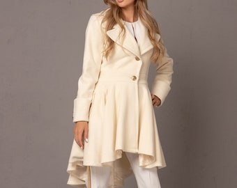 May include: A white coat with a high collar and a high-low hemline. The coat has a button closure and gold buttons. The model is wearing white trousers with a gold stripe down the side.