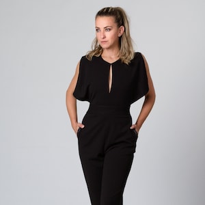 May include: A black jumpsuit with a keyhole neckline and short, wide sleeves. The jumpsuit has a fitted bodice and wide-leg trousers with zipper details at the ankles.