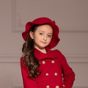 以下が含まれることがあります： 赤いコートと赤い帽子をかぶった若い女の子が、同じ赤いコートを着た小さな犬と一緒に歩いています。犬は床に横たわっています。