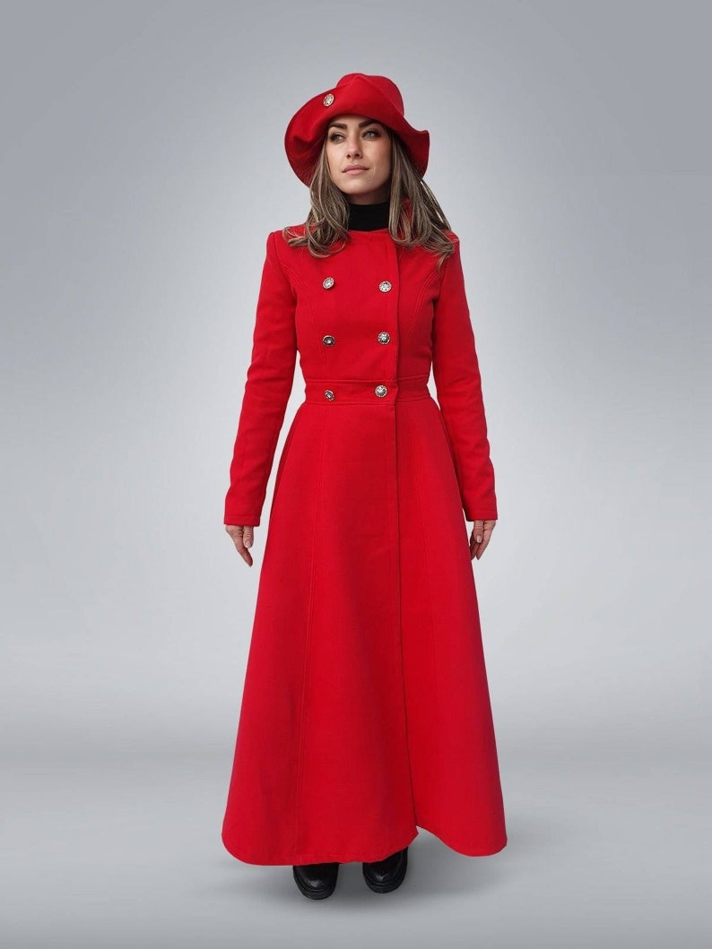 May include: A long red coat with a double breasted closure and a matching red hat. The coat has a fitted bodice and a flared skirt.