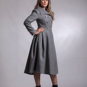 May include: A gray double-breasted coat with gold buttons and a flared skirt. The coat is worn by a person with long brown hair and is standing on a gray background.