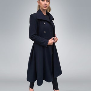 May include: A long, navy blue coat with a high collar and a double-breasted closure. The coat has a flared skirt and is worn with black pants and heels.