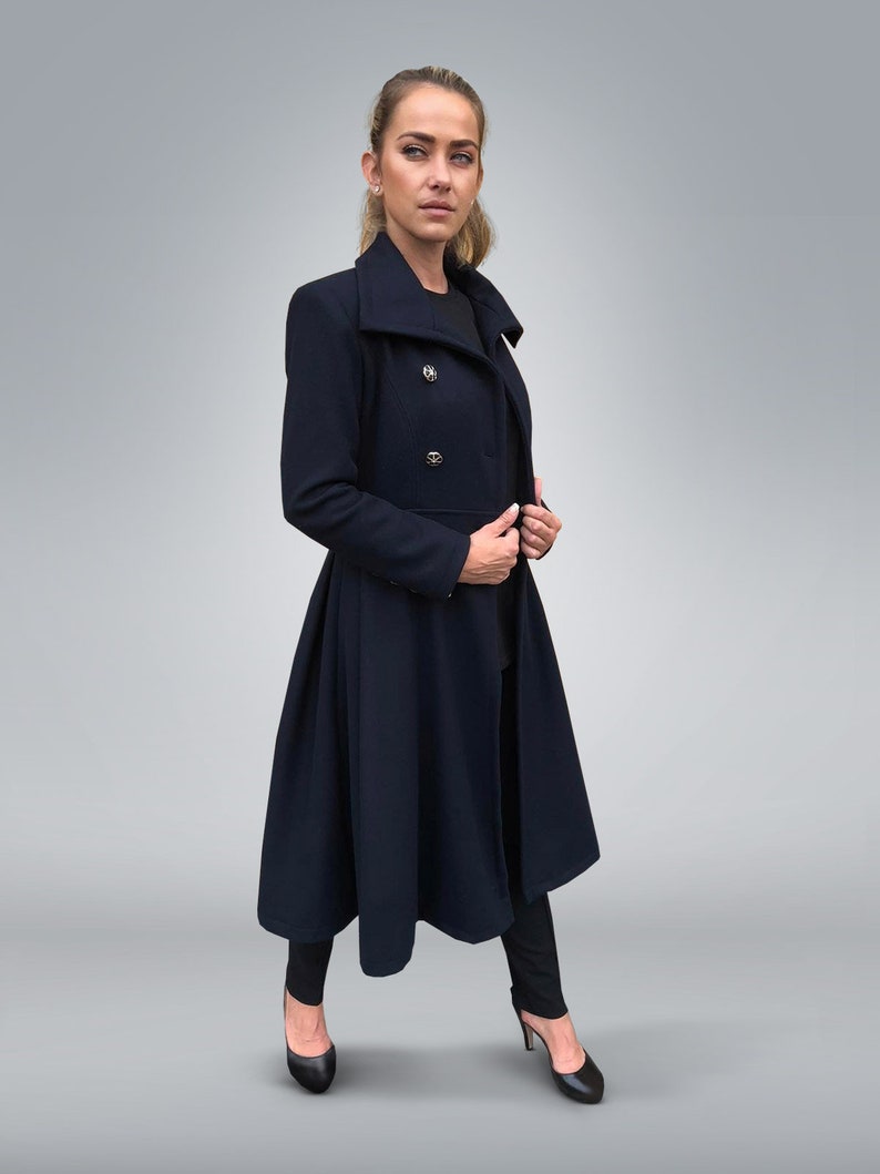 May include: A long, navy blue coat with a high collar and a double-breasted closure. The coat has a flared skirt and is worn with black pants and heels.