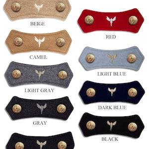 May include: Eight felt fabric mask extenders with gold-tone metal buttons. The extenders are in the colors beige, camel, red, light blue, light gray, gray, dark gray, and black. Each extender has a white embroidered angel wing design.