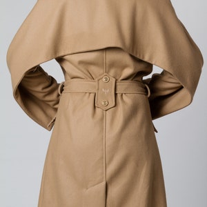 May include: A camel-colored wool coat with a large collar and a belt. The coat has a unique design with the collar extending over the shoulders.