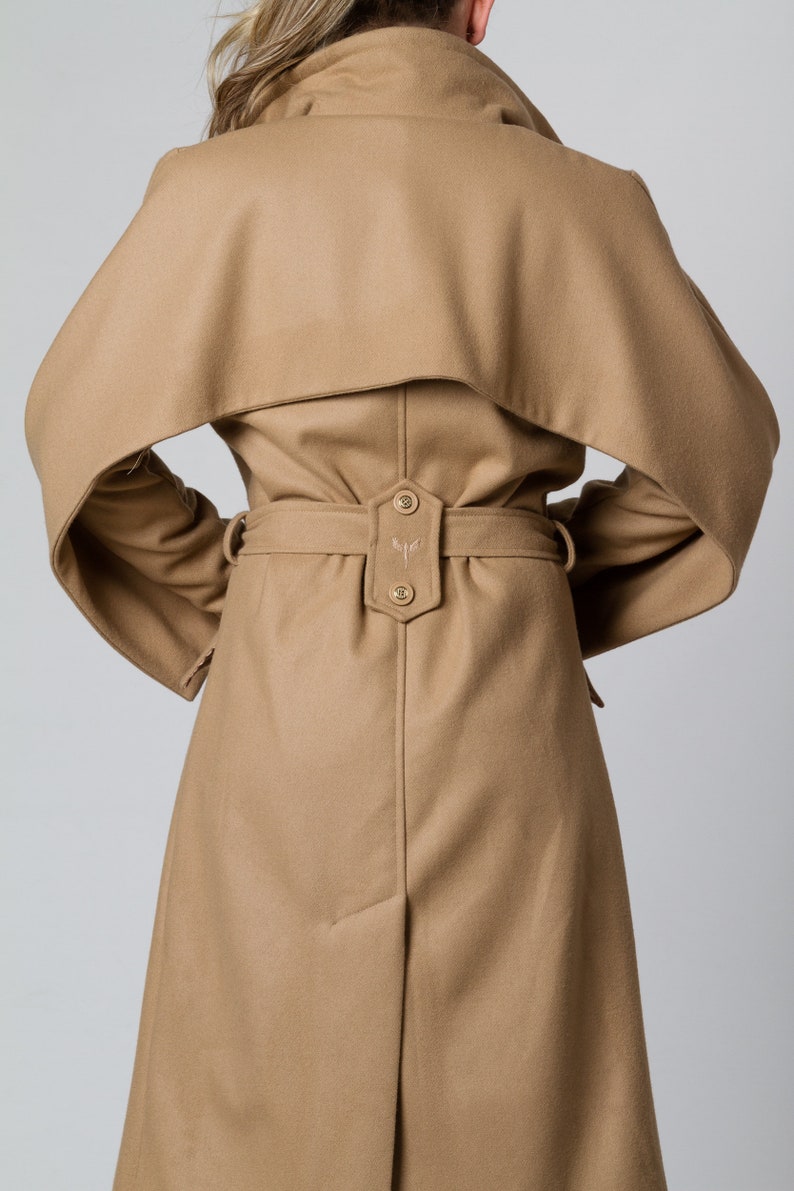 May include: A camel-colored wool coat with a large collar and a belt. The coat has a unique design with the collar extending over the shoulders.