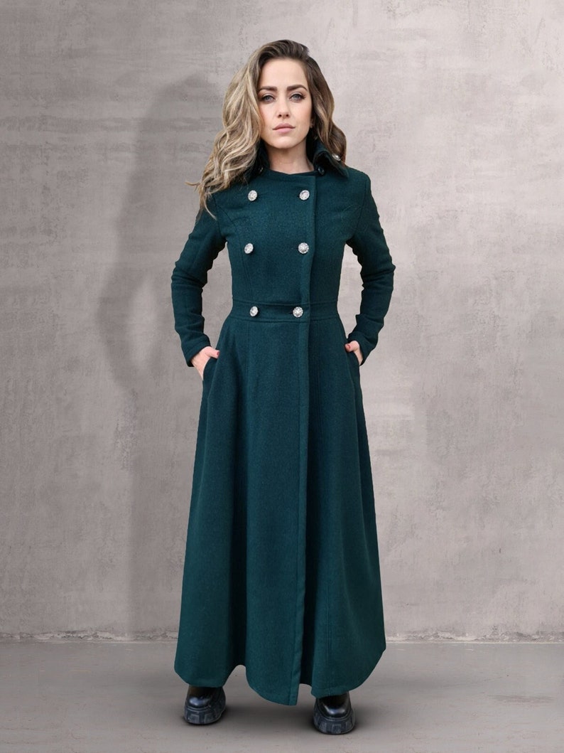 May include: A long, dark green coat with a double-breasted closure and a high collar. The coat has a fitted waist and a flared skirt.