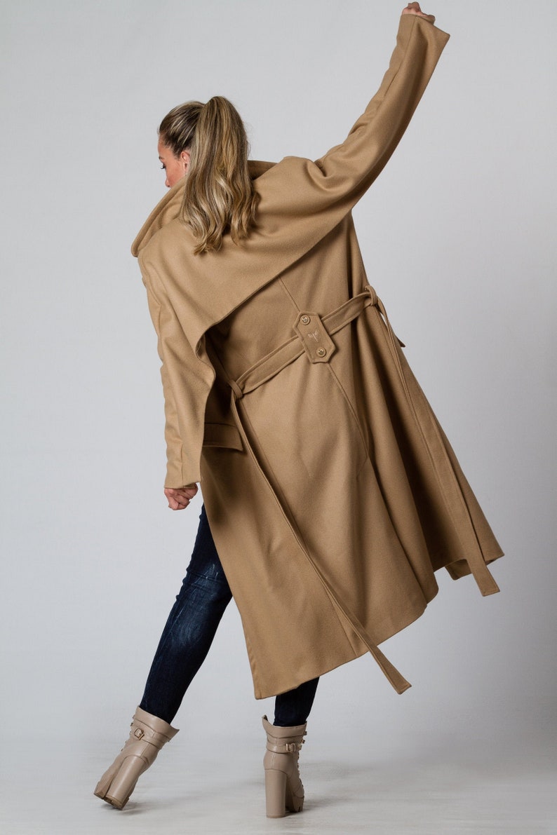 May include: A long camel-colored coat with a wide collar and a belt. The coat has a single button closure and a long, flowing silhouette.