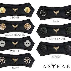 May include: Set of 10 black fabric face mask extenders with different colored buttons. The extenders feature a gold embroidered butterfly design. The buttons include gold, silver, black, and white.