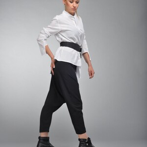 May include: A woman wearing a white button-down shirt with a black belt and black pants. She is wearing black ankle boots.
