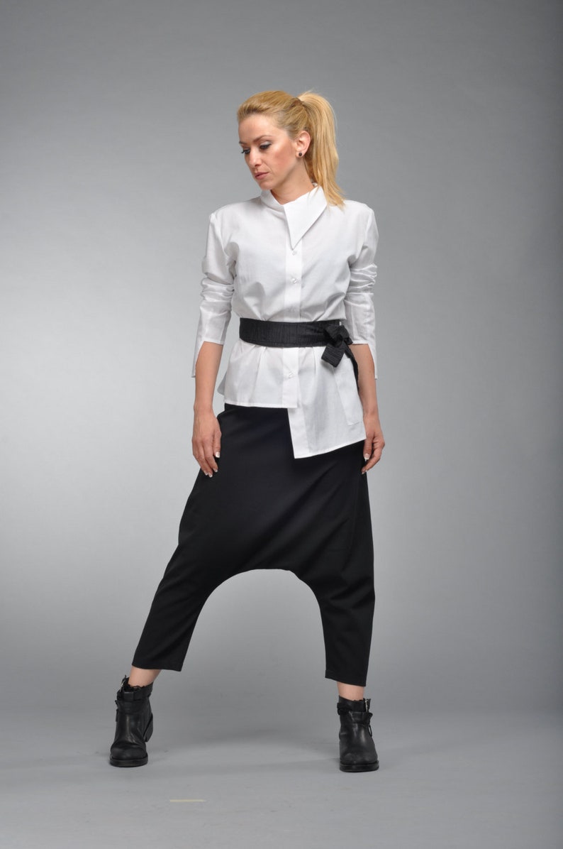 May include: A white button-down shirt with a black belt tied in a bow at the front. The shirt is worn with black, loose-fitting pants.