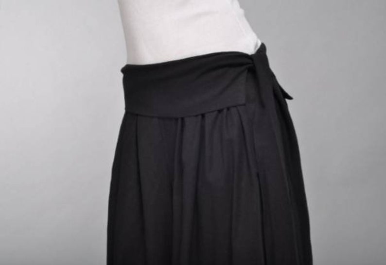 May include: A black skirt with a wide waistband that ties at the front. The skirt is made of a soft, flowing fabric.
