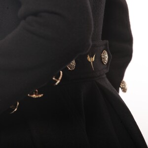 May include: Black coat with gold accents and a decorative belt. The belt has a gold buckle and a gold bird design.