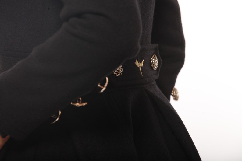 May include: Black coat with gold accents and a decorative belt. The belt has a gold buckle and a gold bird design.