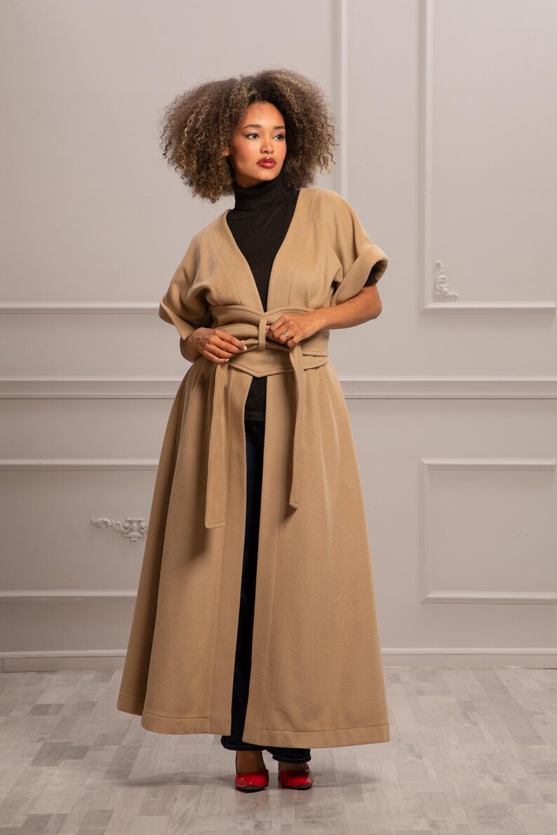 May include: A long, tan coat with a V-neck and a self-tie belt. The coat has short sleeves and a flowing skirt.