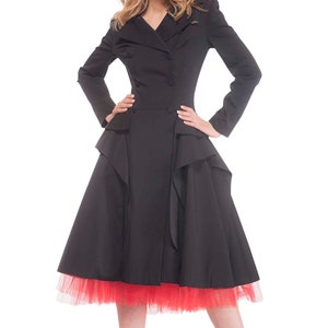 May include: A black coat with a ruffled skirt and a red tulle underskirt. The coat has a double-breasted closure and a collar. The model is wearing red high heels.
