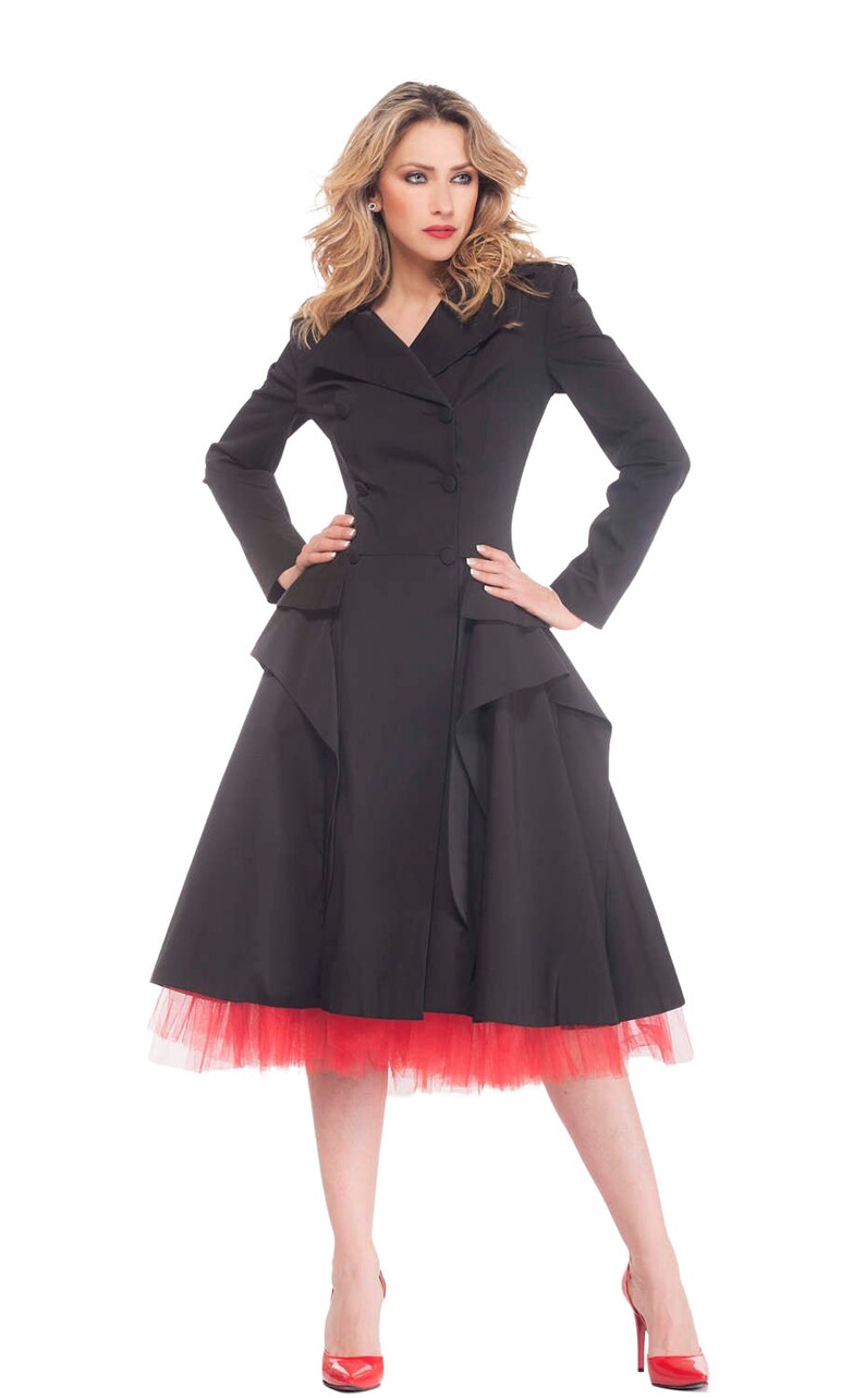 May include: A black coat with a ruffled skirt and a red tulle underskirt. The coat has a double-breasted closure and a collar. The model is wearing red high heels.