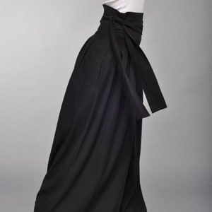 May include: Black wide-leg pants with a high waist and a black fabric belt that ties at the front. The pants have a pleated design and a flowing silhouette.
