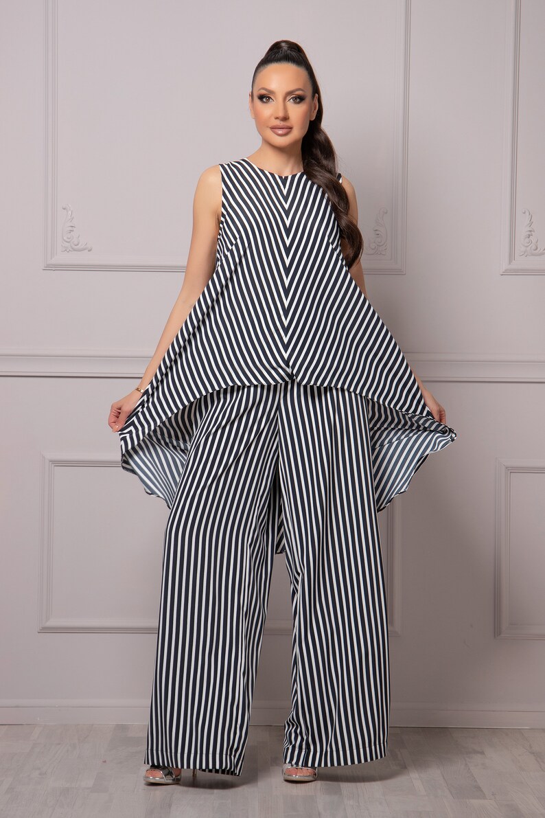 May include: A black and white striped jumpsuit with a high-low hemline. The top of the jumpsuit is sleeveless and has a v-shaped neckline. The pants are wide-legged and flowy.