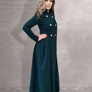 May include: A long, dark green coat with a high collar and button closures. The coat has a fitted bodice and a flowing skirt.