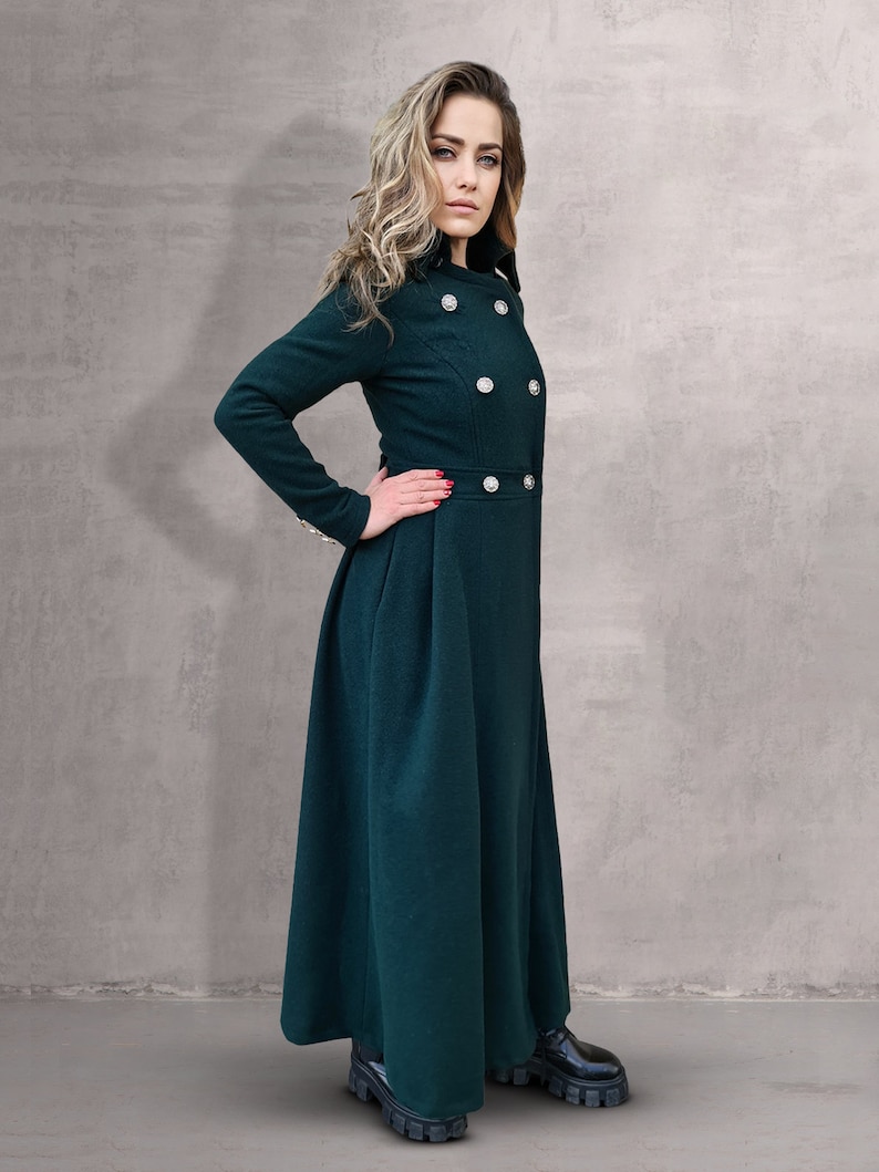 May include: A long, dark green coat with a high collar and button closures. The coat has a fitted bodice and a flowing skirt.