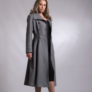 May include: A gray long coat with a double breasted closure and gold buttons. The coat has a fitted waist and a flared skirt. The model is wearing black boots.