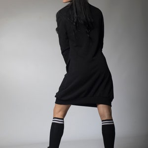 May include: A woman wearing a black long-sleeved dress with a loose fit and white striped knee-high socks. She is wearing black platform boots and has long black hair.