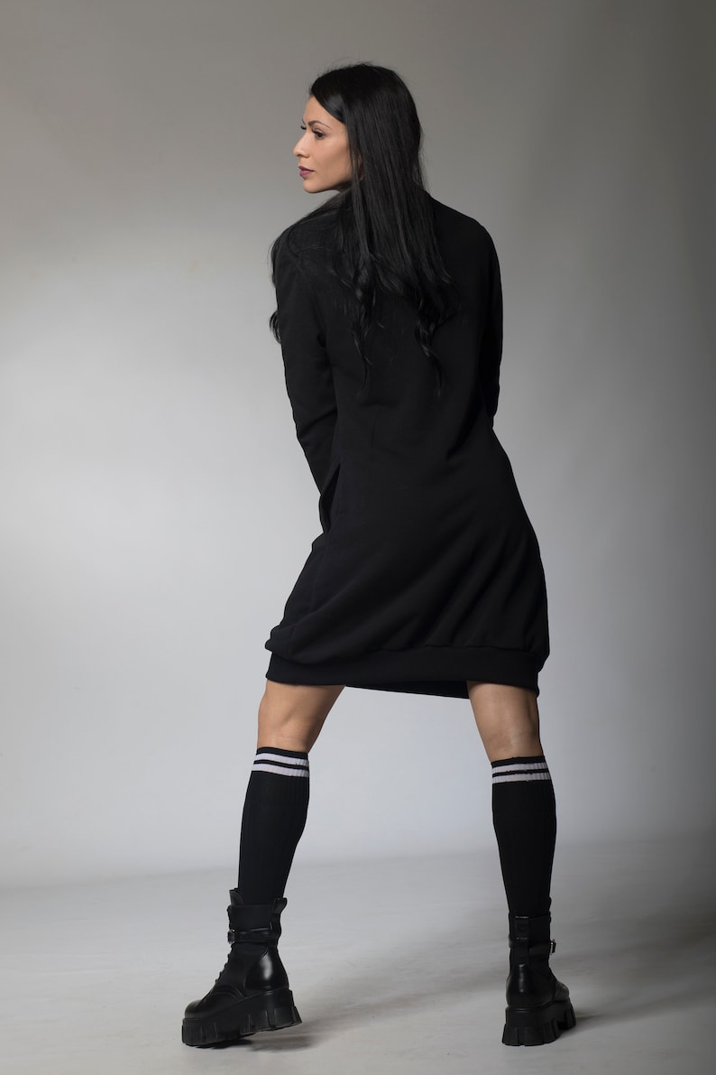 May include: A woman wearing a black long-sleeved dress with a loose fit and white striped knee-high socks. She is wearing black platform boots and has long black hair.