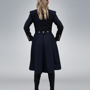 May include: A black long-sleeved coat with a high collar, gold buttons, and a fitted waist. The coat has a flared skirt and is worn by a person with long blonde hair.