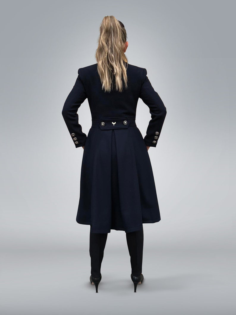 May include: A black long-sleeved coat with a high collar, gold buttons, and a fitted waist. The coat has a flared skirt and is worn by a person with long blonde hair.