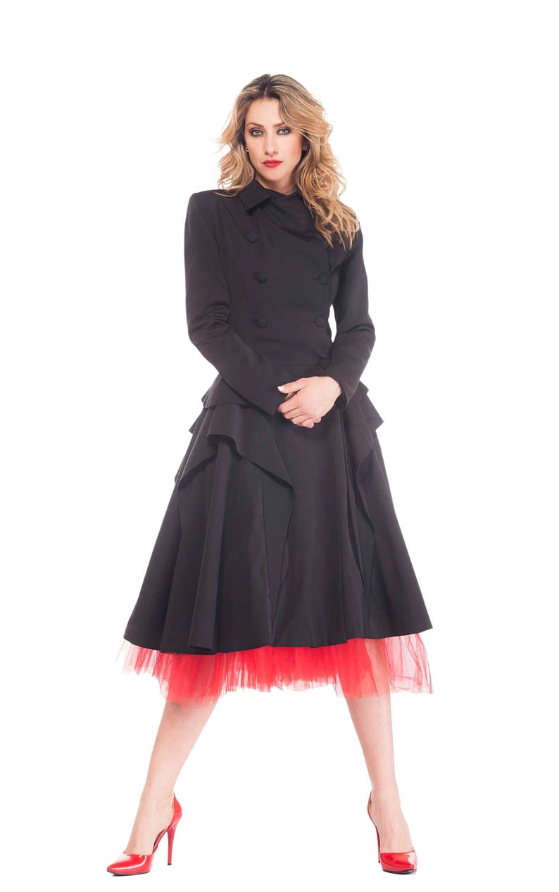 May include: A woman wearing a black double-breasted coat with a ruffled skirt and a red tulle underskirt. She is wearing red high heels.