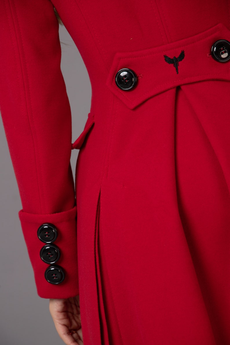 May include: A red long coat with a black bird embroidered on the back. The coat has a double breasted closure with black buttons and a single button on each cuff.