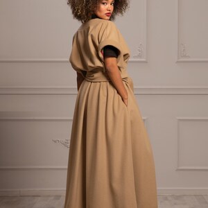 May include: A long, tan coat with a belted waist and a wide skirt. The coat has a simple, elegant design and is made of a soft, luxurious fabric.
