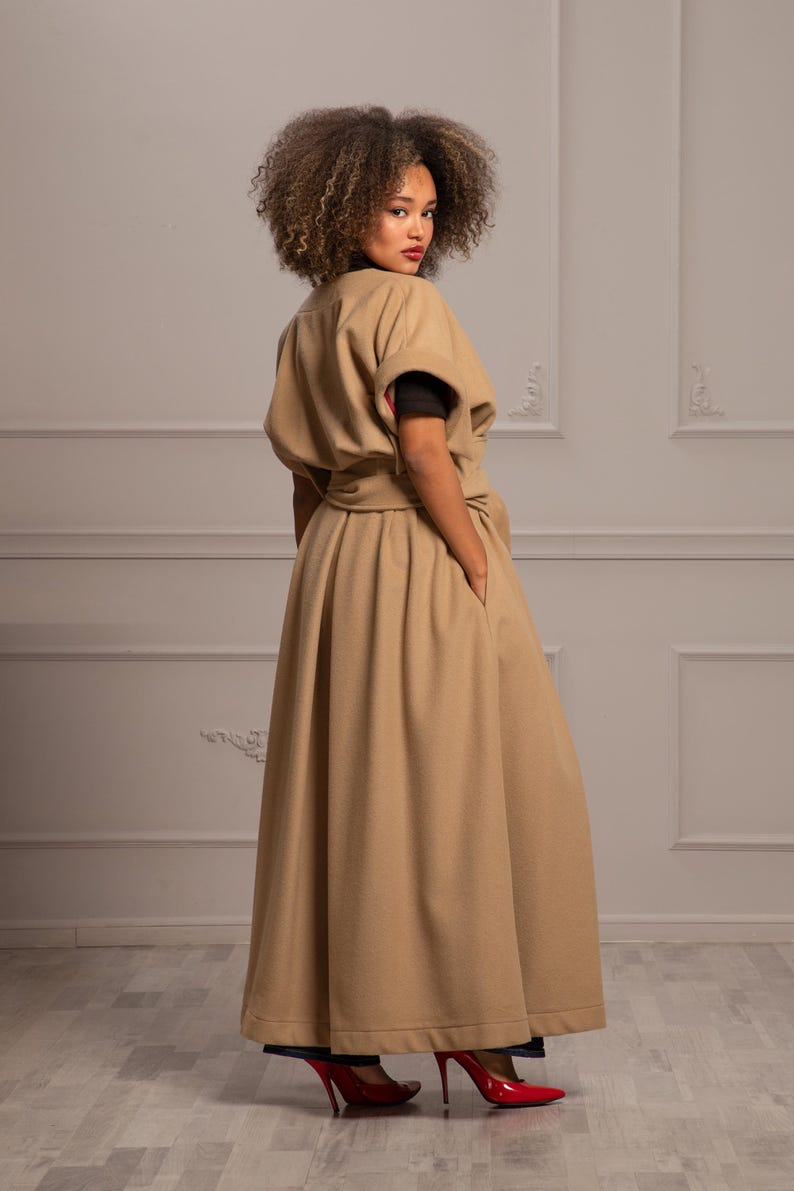 May include: A long, tan coat with a belted waist and a wide skirt. The coat has a simple, elegant design and is made of a soft, luxurious fabric.