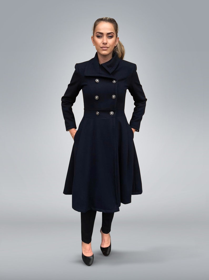 May include: A navy blue double-breasted coat with a high collar and a flared skirt. The coat has gold buttons and is worn by a woman with a ponytail.