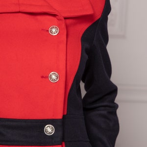 May include: A red and navy blue coat with a contrasting color block design. The coat has a large collar and three silver buttons.
