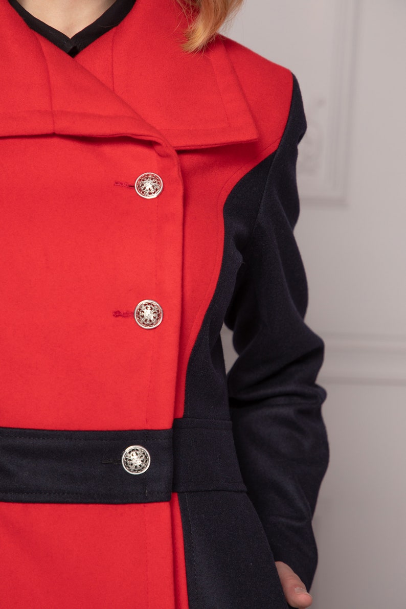 May include: A red and navy blue coat with a contrasting color block design. The coat has a large collar and three silver buttons.