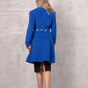 May include: A royal blue long coat with a belt and gold buttons. The coat has a flared skirt and is worn over a black skirt.