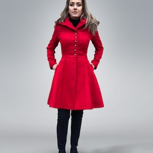 May include: A vibrant red coat with a flared skirt, featuring silver buttons down the front and a tailored waist. The coat is paired with black pants and sneakers. The person is standing in front of a light gray background.