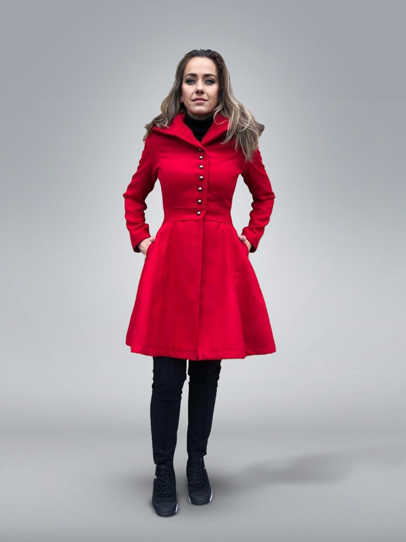 May include: A vibrant red coat with a flared skirt, featuring silver buttons down the front and a tailored waist. The coat is paired with black pants and sneakers. The person is standing in front of a light gray background.