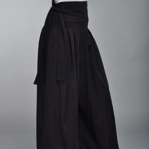 May include: Black wide-leg pants with a wide black waistband that ties at the front. The pants have a flowing, loose fit.