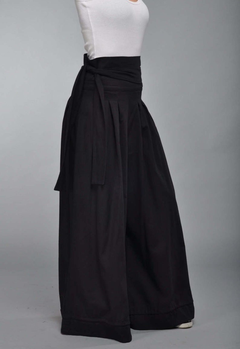 May include: Black wide-leg pants with a wide black waistband that ties at the front. The pants have a flowing, loose fit.