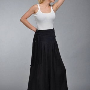 May include: A woman wearing a white tank top and black wide-leg pants with a tie at the waist.