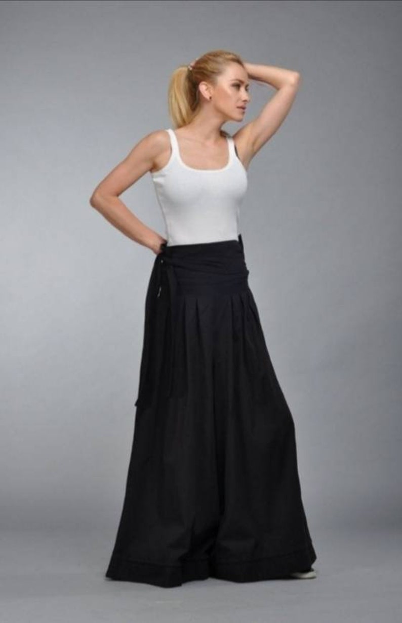 May include: A woman wearing a white tank top and black wide-leg pants with a tie at the waist.